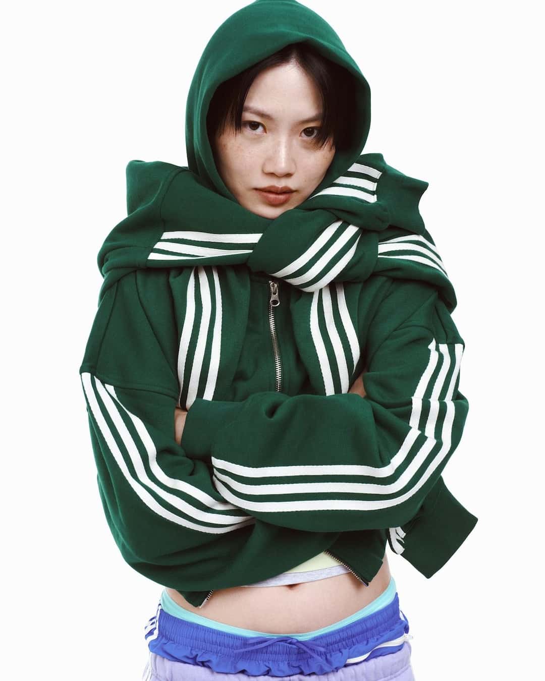 Mujer con una campera verde con tres tiras blancas y la capucha puesta, de la colección adiSignature de adidas Originals