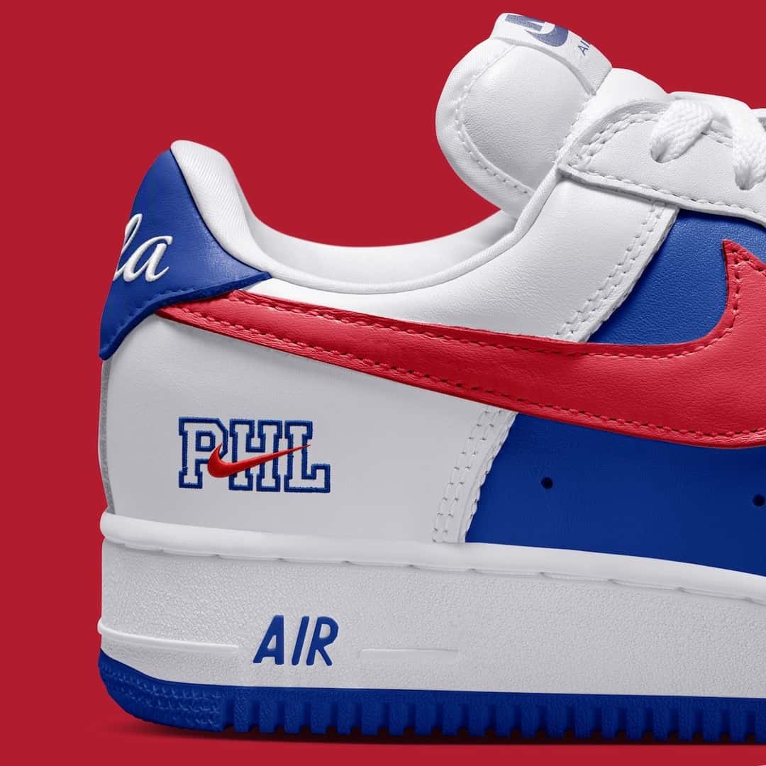 Detalle del talón de la Nike Air Force 1 '01 Philly sobre fondo rojo, con las letras PHL en azul atravesadas por un Swoosh rojo, el Swoosh rojo grande del lateral y la palabra AIR en la mediasuela