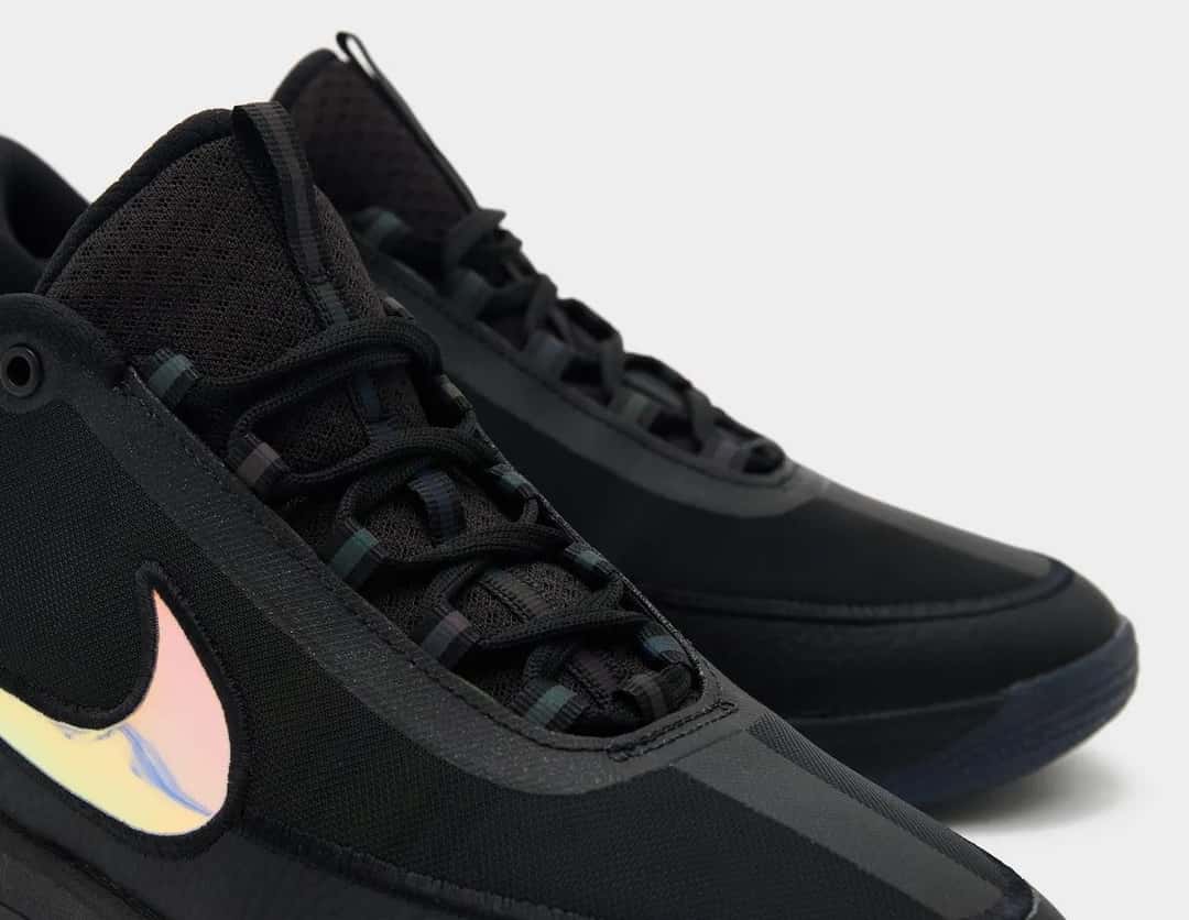 Primer plano del Nike Book 2 Desert Night con el Swoosh iridiscente sobre la capellada negra y los cordones negros