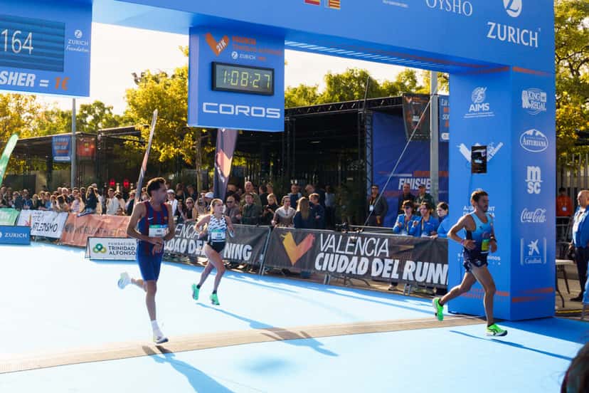 Laura Luengo, de top blanco, llega a la meta del Medio Maratón de Valencia entre dos corredores