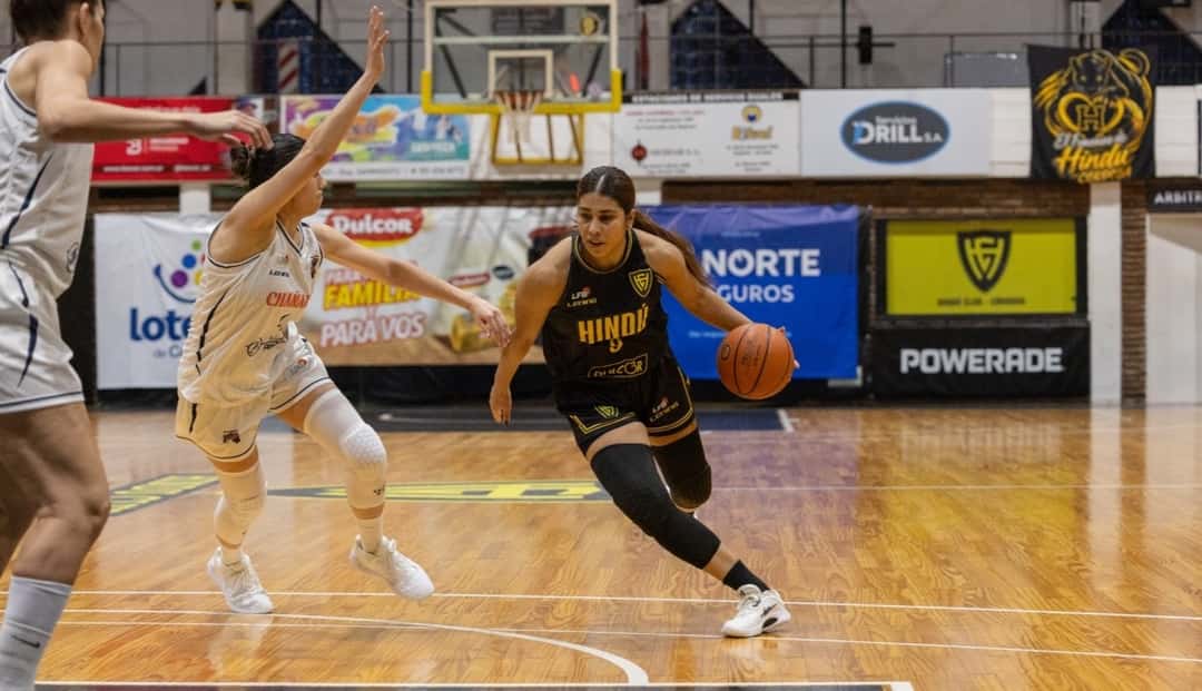 Una jugadora de Hindú, con camiseta negra y amarilla, avanza con la pelota ante una rival de Chañares, de blanco, en La Catedral
