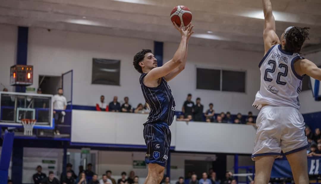 Un jugador de Argentino, con camiseta azul oscura a rayas, lanza ante la marca de un rival de camiseta blanca