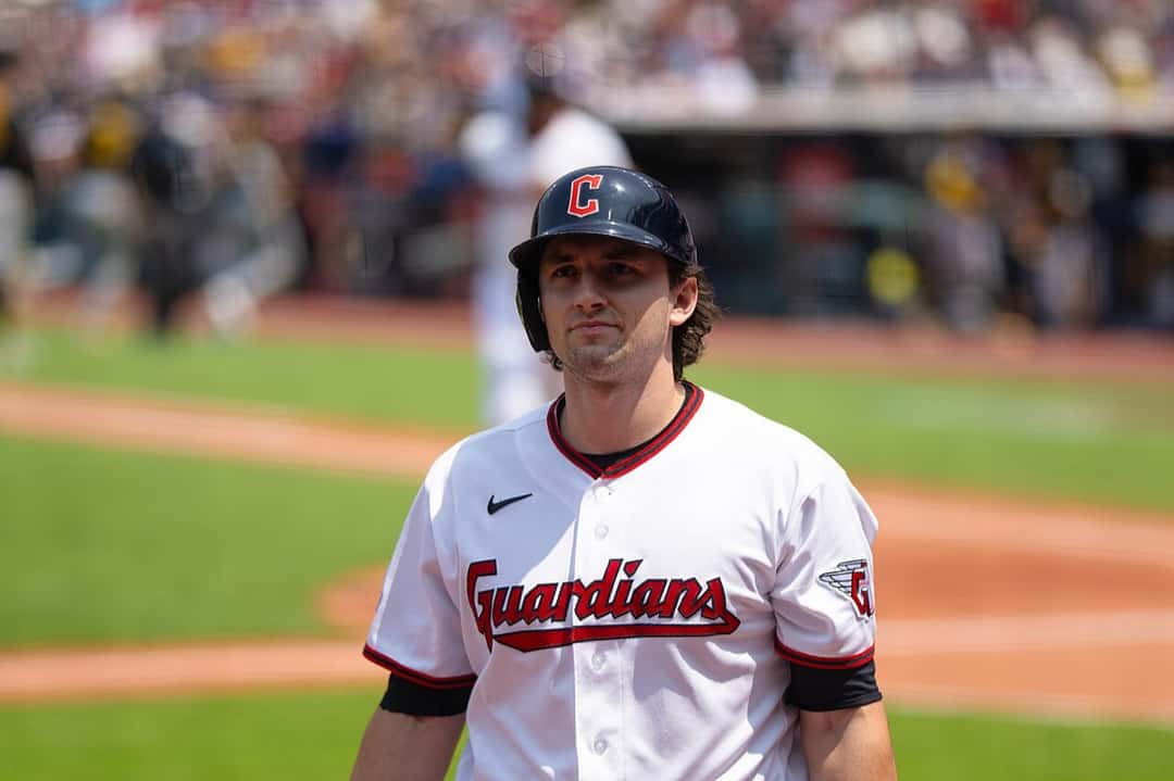 Foto de archivo: Chase DeLauter, de los Cleveland Guardians, con casco azul con la C roja y camiseta blanca, caminando por el campo con la tribuna desenfocada detrás