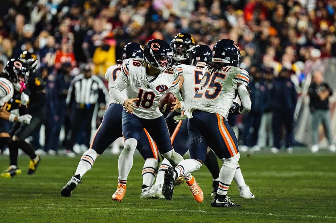 Foto de archivo: Caleb Williams, con la camiseta blanca número 18 de los Bears y casco azul, sostiene la pelota rodeado de compañeros durante una jugada