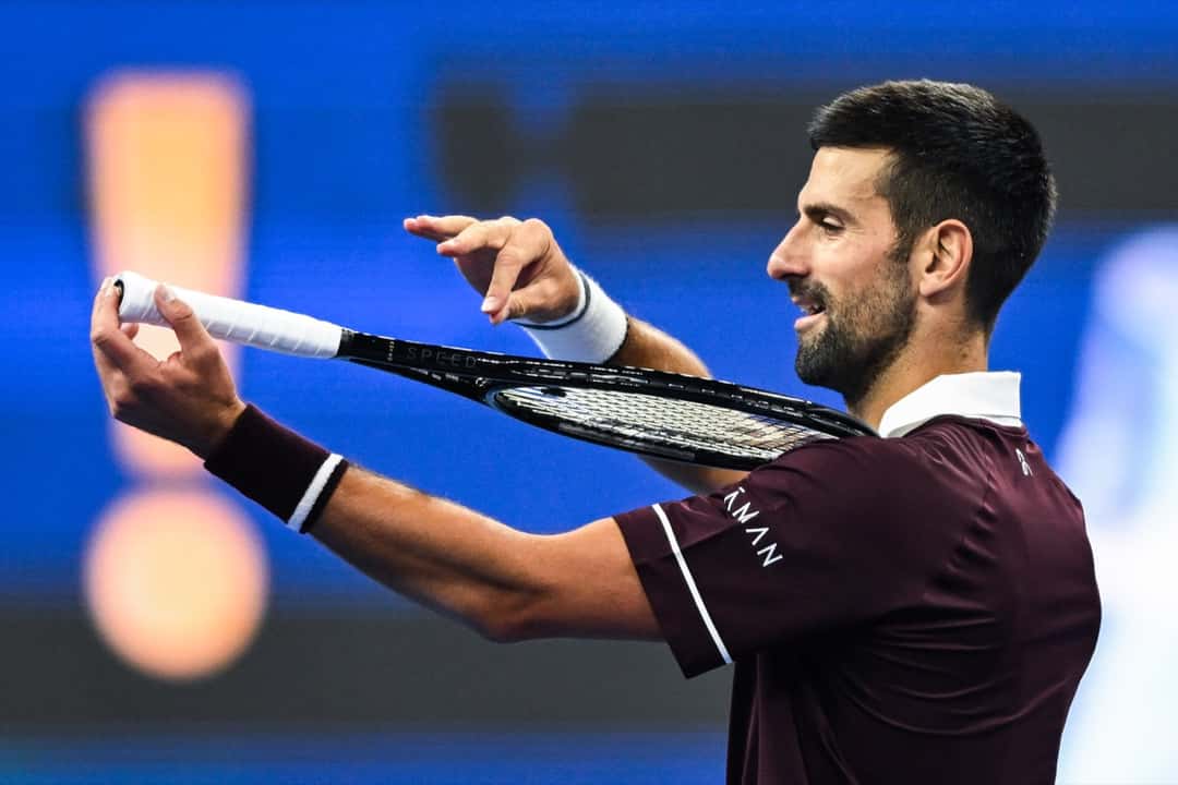 Novak Djokovic, de remera bordó, mira y acomoda su raqueta con las dos manos en la cancha del China Open 2026, durante su partido de cuartos de final
