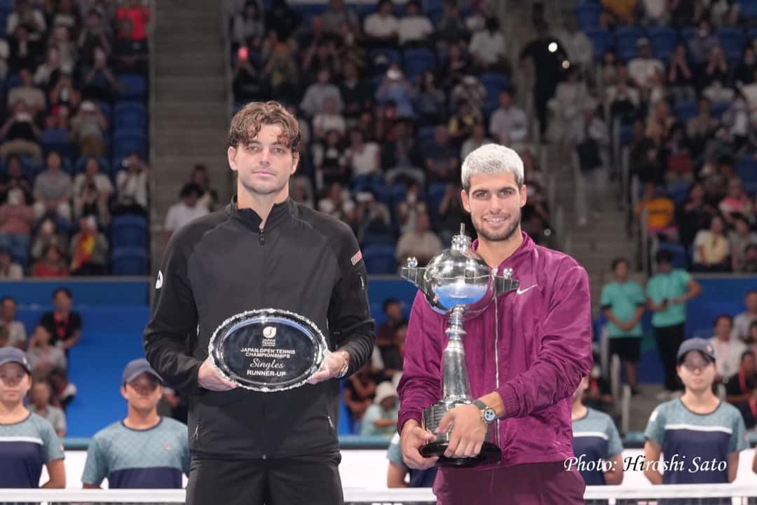 Foto de archivo: Carlos Alcaraz, con campera bordó, sostiene el trofeo de campeón del Japan Open 2025 junto a Taylor Fritz, de negro, con la bandeja de subcampeón