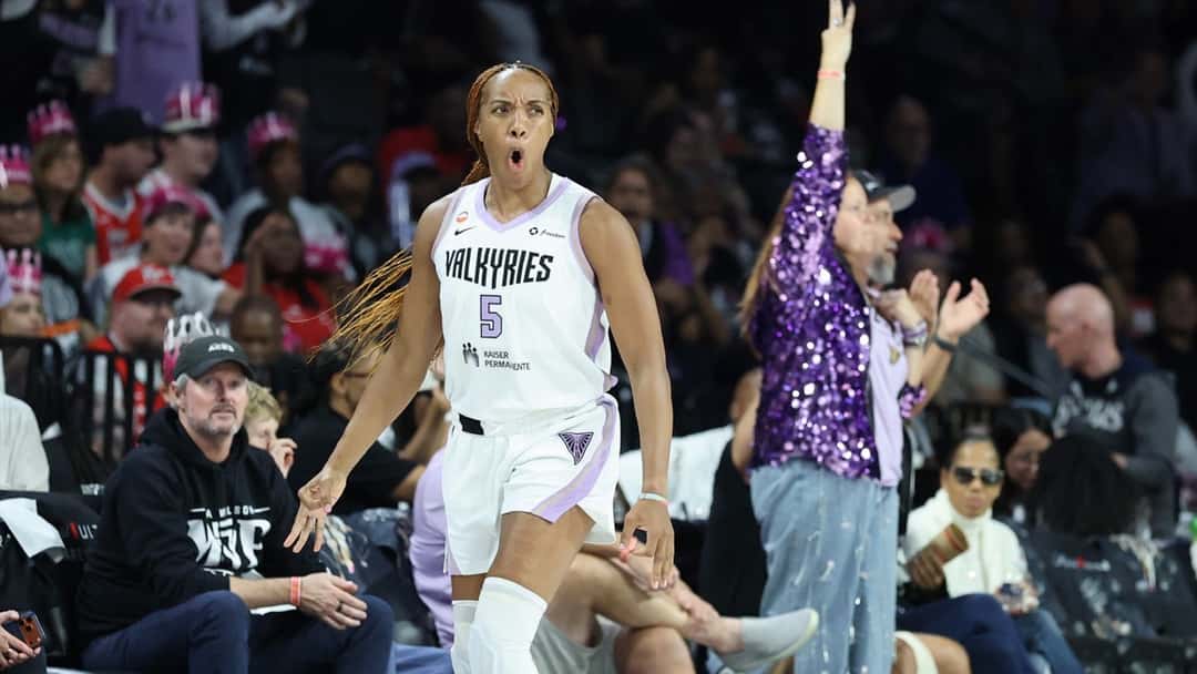 Kayla Thornton, con la camiseta blanca número 5 de Golden State Valkyries, grita y festeja un triple frente a la tribuna, con una hincha vestida de violeta aplaudiendo atrás