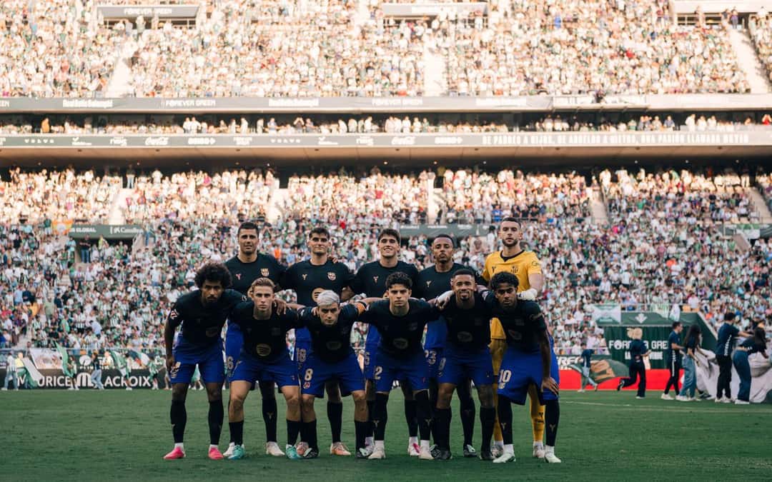 Los once titulares del Barcelona, con la camiseta azul oscura y pantalón azul, posan para la foto de equipo antes del partido en La Cartuja, con la tribuna llena detrás (foto: prensa FC Barcelona)