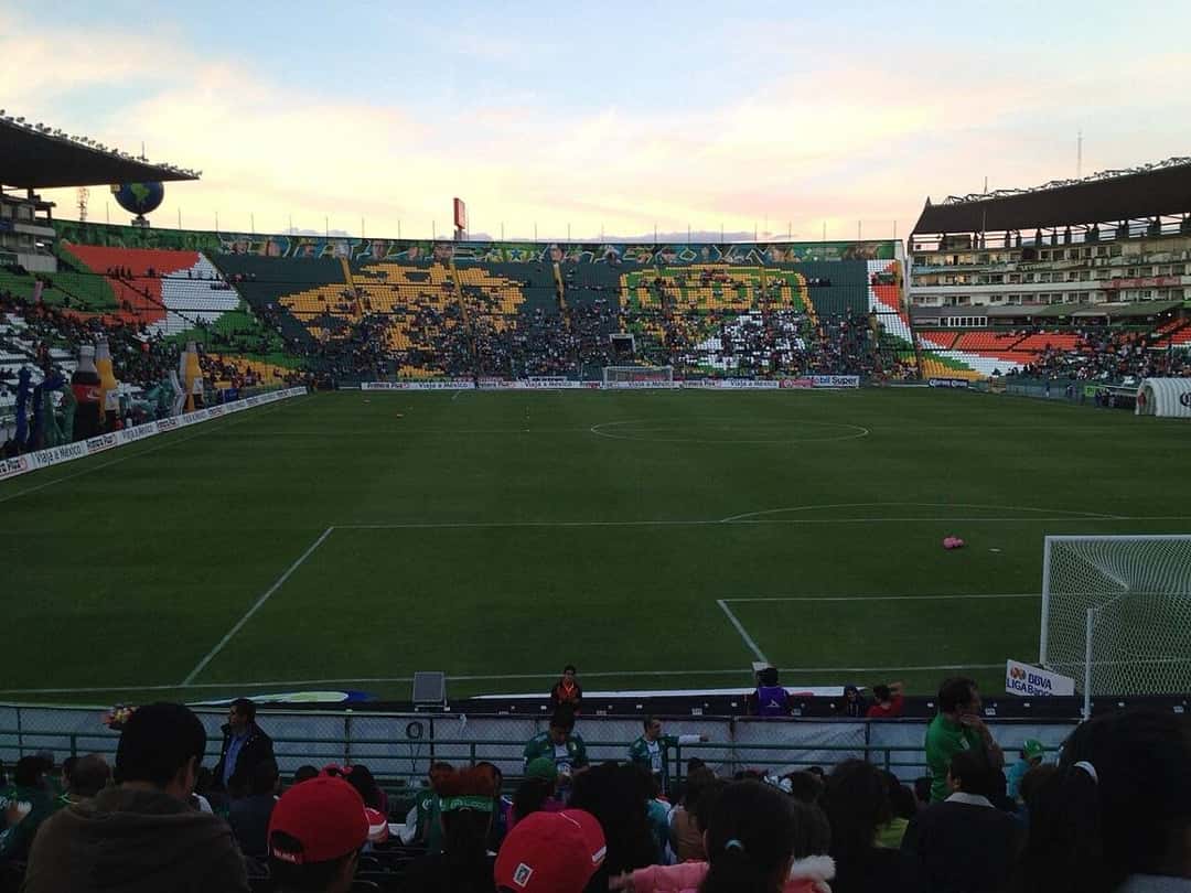La cancha del estadio León vista desde la tribuna, con el mosaico de hinchas verdes en la cabecera al atardecer; foto de archivo de 2013 (foto: Anthnkn, Wikimedia Commons, licencia CC BY-SA 3.0)
