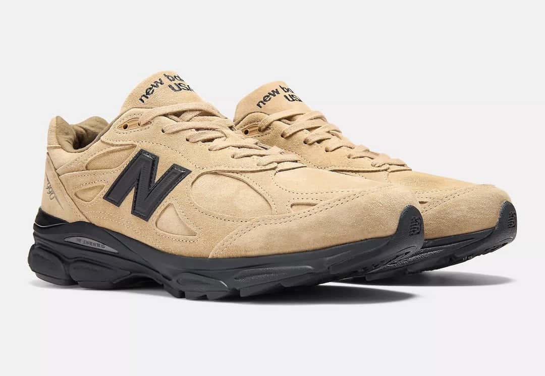 Par del JJJJound x New Balance 990v3 Tan Suede en vista de tres cuartos, con la gamuza tan, la N negra y la lengüeta con la leyenda new balance USA