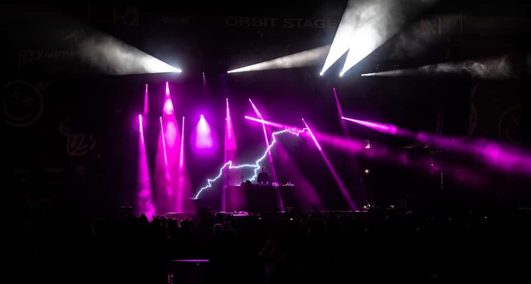 Boys Noize pasa música en la cabina del escenario Orbit Stage del festival Rock am Ring 2022, con haces de luz violeta y un rayo de neón detrás, frente al público a oscuras (foto de archivo). Foto: Andreas Lawen, Fotandi, CC BY-SA 4.0, vía Wikimedia Commons