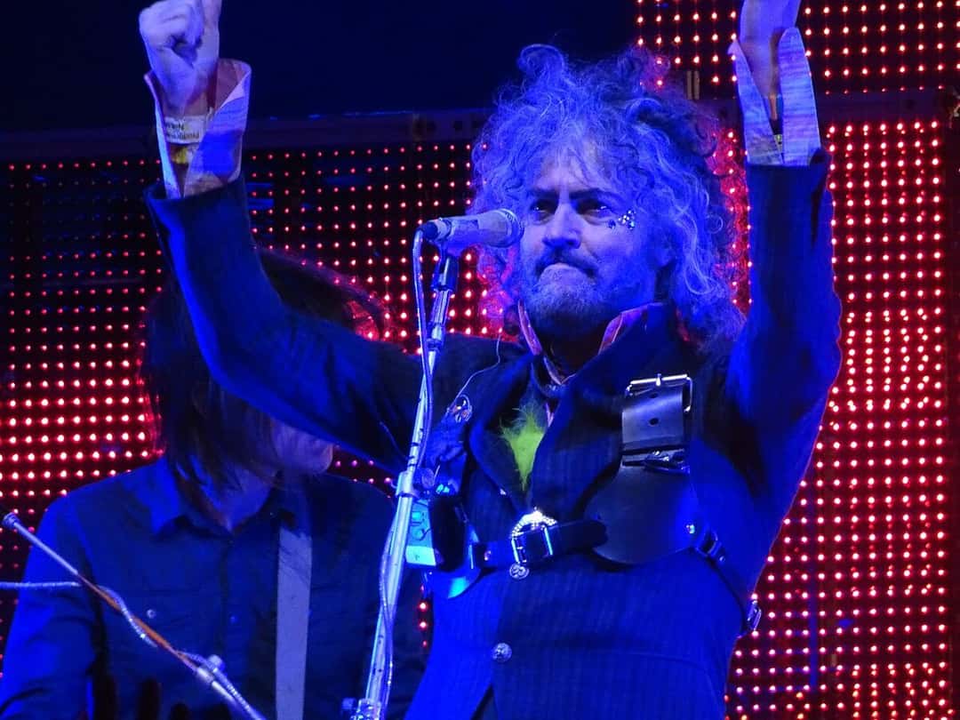 Wayne Coyne, cantante de The Flaming Lips, con los brazos en alto frente al micrófono y una pantalla de luces rojas detrás, en un show de 2017 (foto de archivo). Foto: dom fellowes, CC BY 2.0, vía Wikimedia Commons