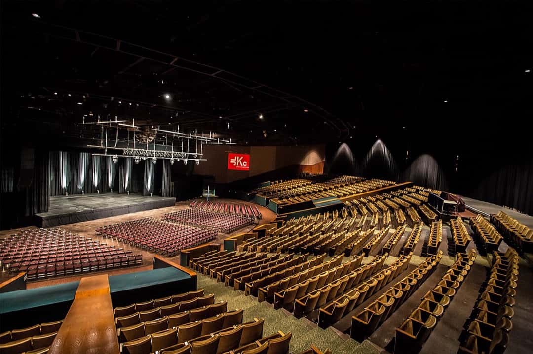 Interior del teatro del James L. Knight Center de Miami visto desde un costado: las plateas con butacas bordó frente al escenario y, a la derecha, las gradas con butacas doradas que suben en escalones. Foto: Gpaz0827, Wikimedia Commons, CC BY-SA 4.0