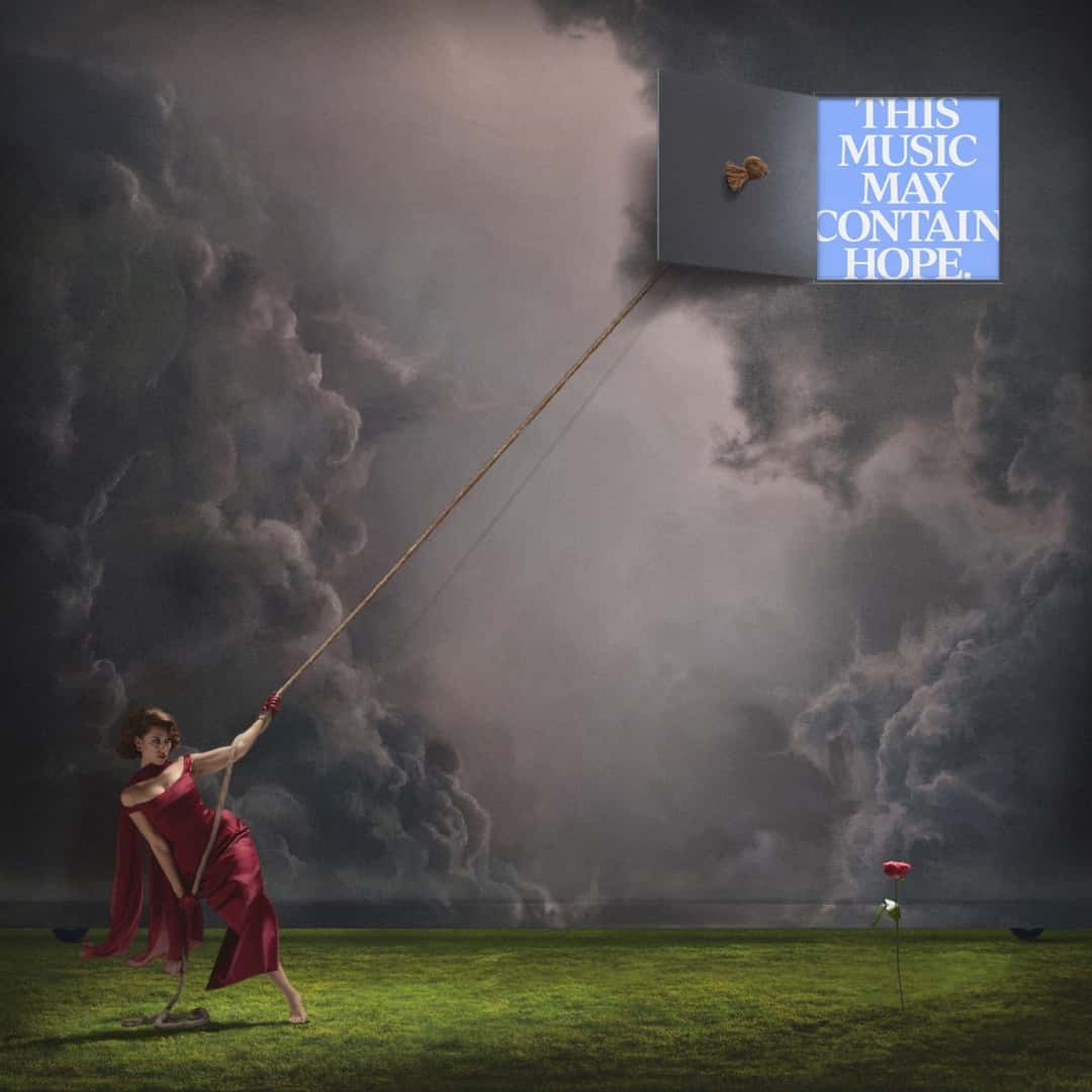 Portada de «THIS MUSIC MAY CONTAIN HOPE.»: Raye con vestido rojo tira de una soga que abre una puerta en un cielo de nubes oscuras, donde aparece el título en letras blancas sobre un recuadro celeste, con una rosa roja sobre el pasto