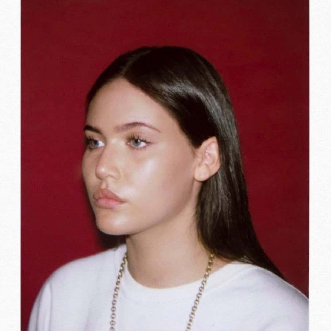Portada del single «NEED ME», de Sienna Spiro, de 2024: la cantante de perfil, con remera blanca y una cadena dorada, frente a un fondo rojo oscuro