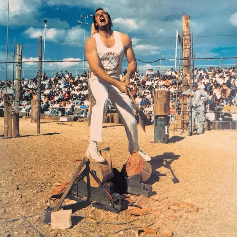 Imagen oficial del anuncio de «Half Cut», de The Chats: una foto de época de un hachero con musculosa blanca que grita mientras corta un tronco en una competencia, frente a una tribuna llena de gente