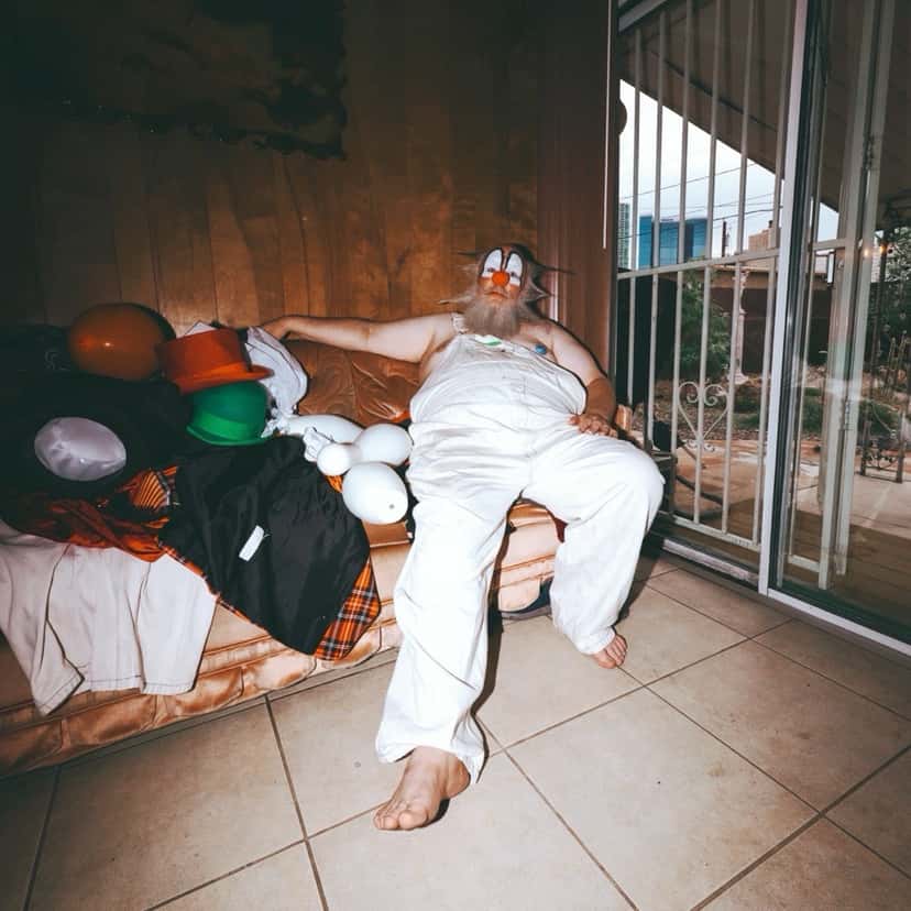 Portada del single «Yiccen», de Wiz Khalifa: un hombre vestido de blanco recostado en un sillón junto a globos de colores, en una habitación con rejas en la ventana