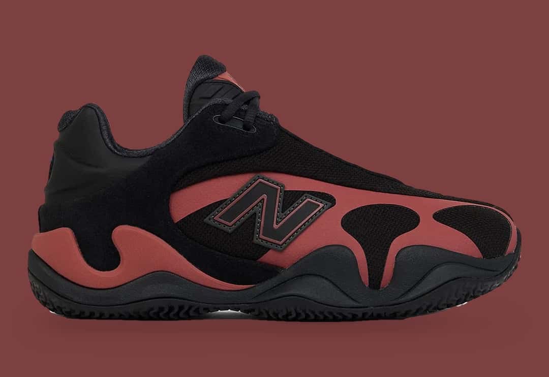 New Balance Maxey V1 Red Rock de perfil, con la N negra de borde rojo y la jaula lateral en rojo ladrillo