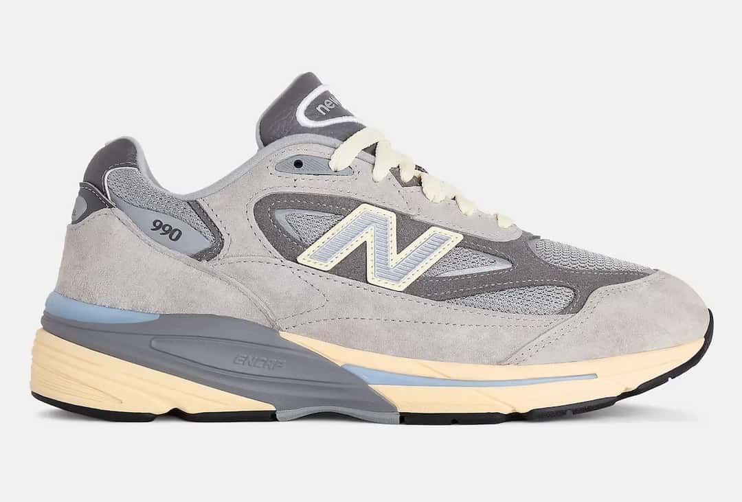 New Balance 990v7 Kool Grey de perfil, el primer color del modelo, con gamuza en dos grises, malla gris y la N celeste con borde amarillo