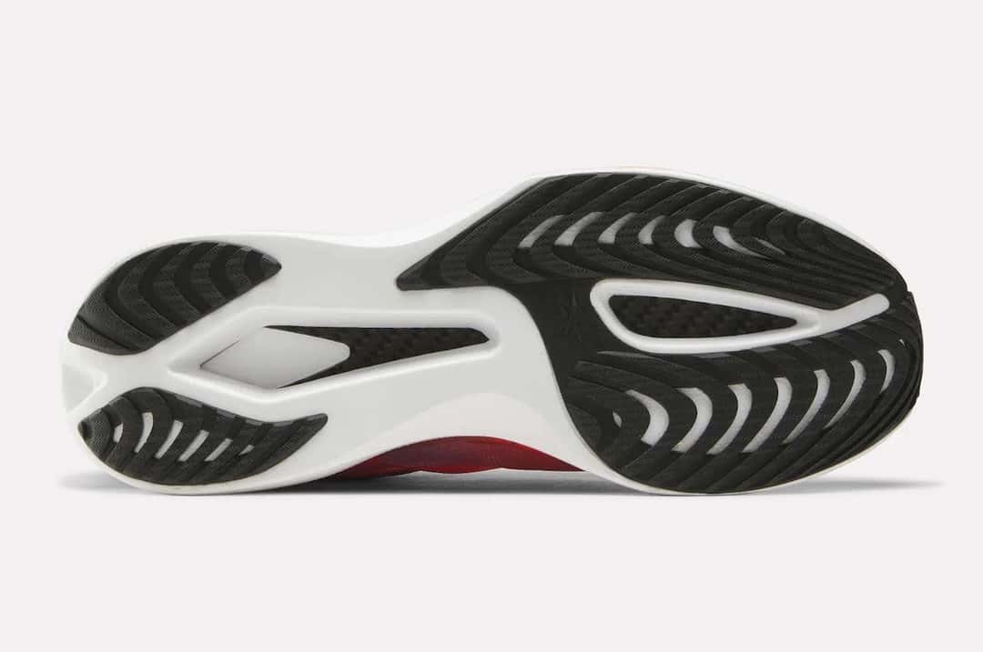 Suela de la Reebok SpeedShifter con tres sectores de goma negra con dibujo en espiga sobre la espuma blanca, y la placa de carbono a la vista en los dos huecos centrales