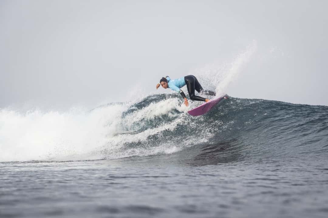 Sol Aguirre gira sobre una ola con la lycra celeste de competencia y una tabla violeta