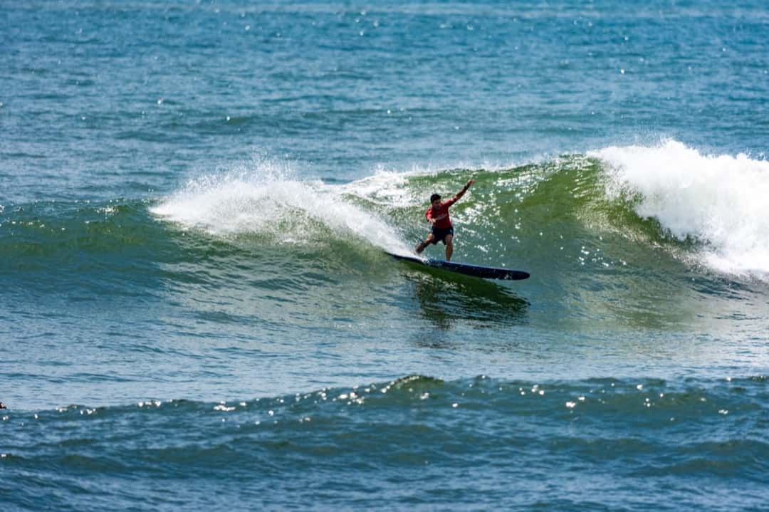 Piccolo Clemente gira con su longboard sobre una ola verde de El Sunzal, con la lycra roja de competencia