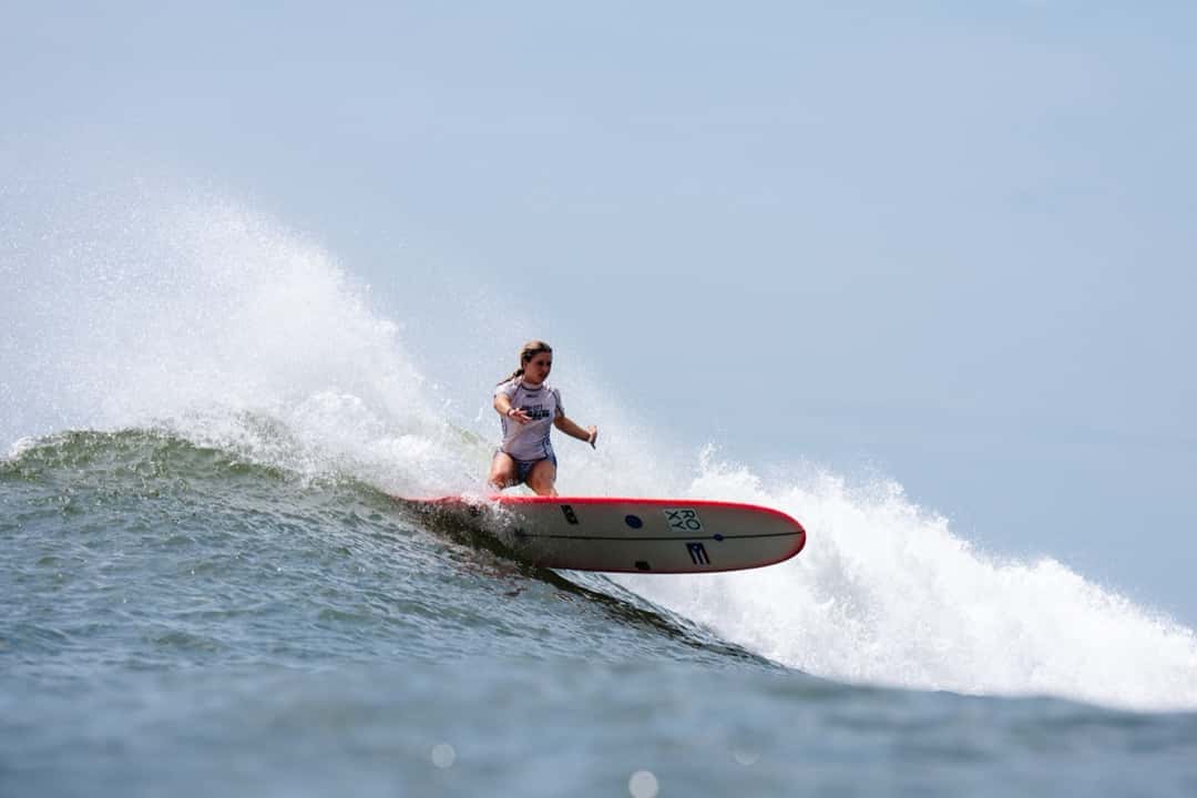 Estorya Martinez, con lycra blanca, gira sobre un longboard rojo y blanco en el labio de una ola de El Sunzal