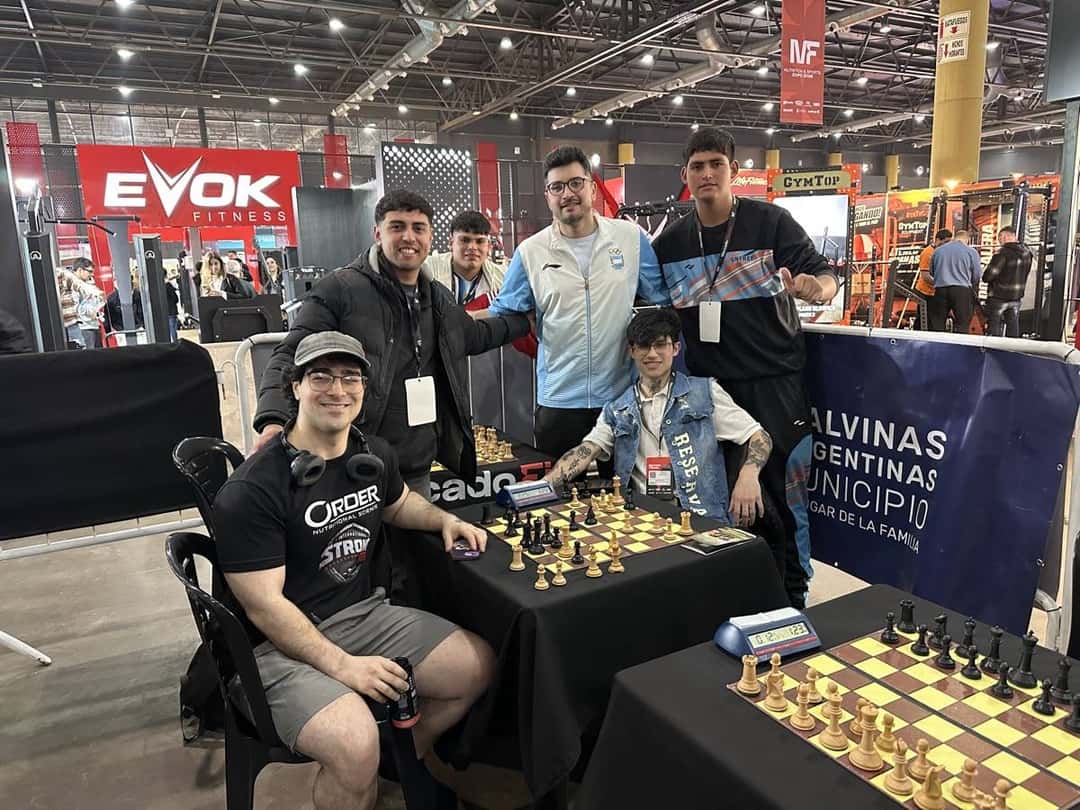 Dos jugadores con remeras de la selección argentina juegan una partida de ajedrez con reloj, rodeados de otros participantes, en el stand de los JAUR en la Expo Fitness (foto de archivo)