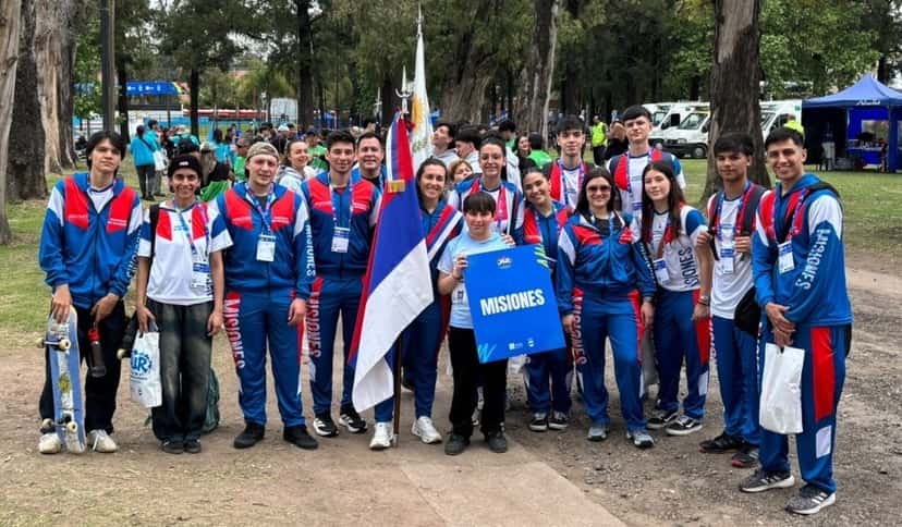 La delegación de Misiones posa con la bandera provincial y el cartel de la provincia en el predio de los Juegos Argentinos Urbanos; a la izquierda, un deportista sostiene una tabla de skate