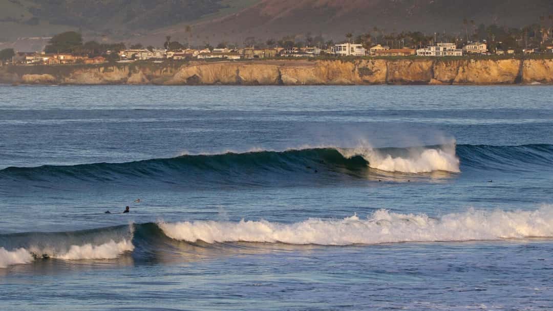 Olas rompiendo frente a los acantilados y las casas de la costa de Pismo Beach, en California, con un surfista remando en el agua