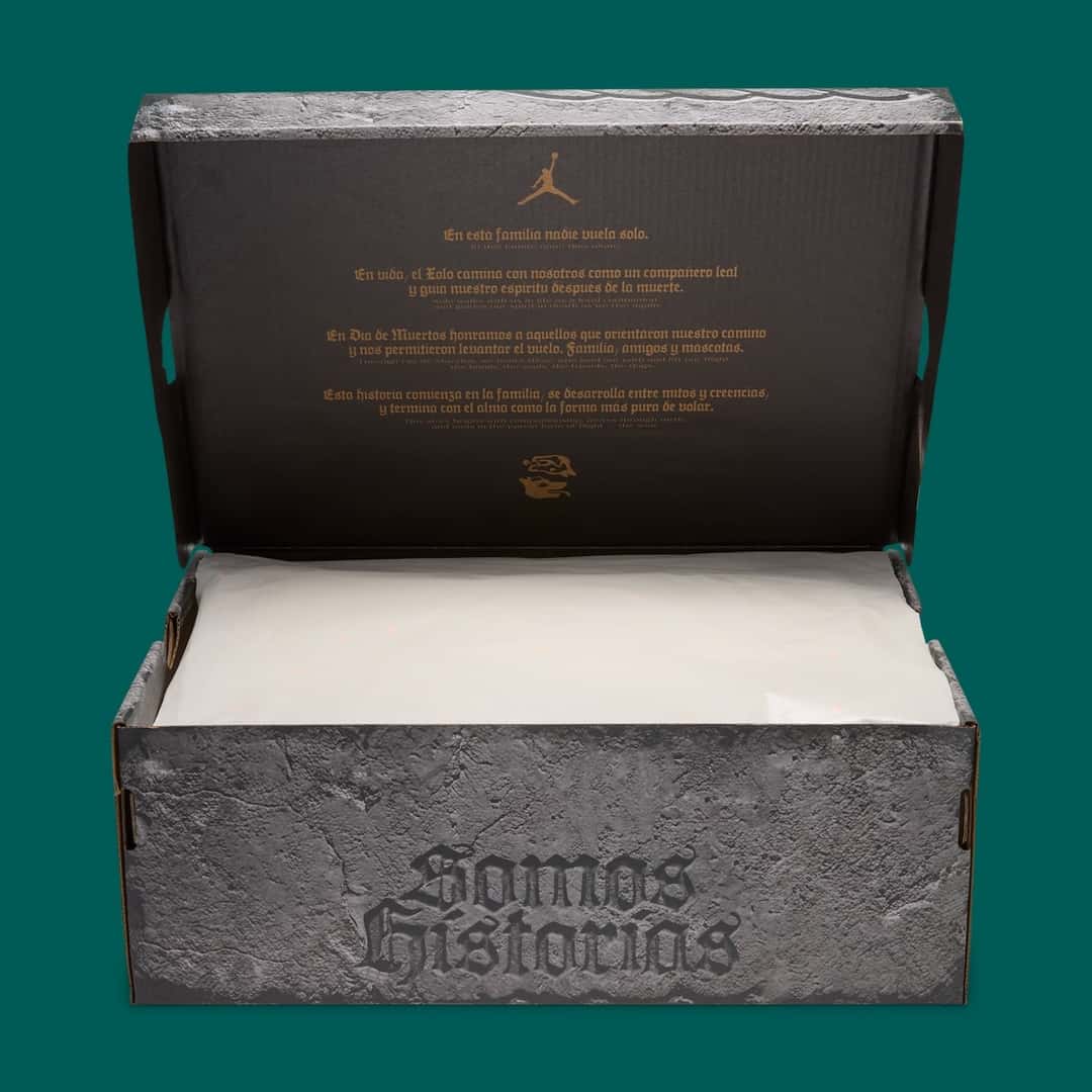Caja del Air Jordan 1 Low OG Somos Historias abierta sobre fondo verde petróleo, con estampado de piedra gris, las letras góticas Somos Historias al frente y la tapa interior negra con un texto dorado sobre el Xolo y el Día de Muertos