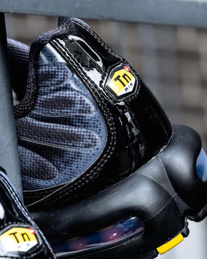 Detalle del talón del Nike Air Max Plus negro y gris con la pieza de charol negro, la malla con puntos y el logo Tn amarillo
