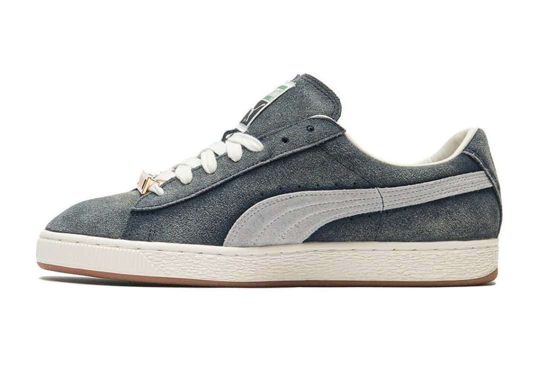 A$AP Rocky x PUMA Suede '94 Faded Blue de perfil sobre fondo blanco, con gamuza azul gastada, Formstrip gris, cordones blancos, chapita dorada y mediasuela blanca con suela de goma marrón