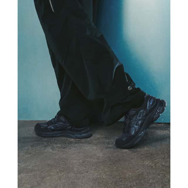 Foto de campaña de la ASICS Utility Collection con el GEL-NYC 2.0 GTX en negro, con detalles en gris oscuro y un toque azul en el talón, usado con un pantalón cargo negro sobre fondo azul