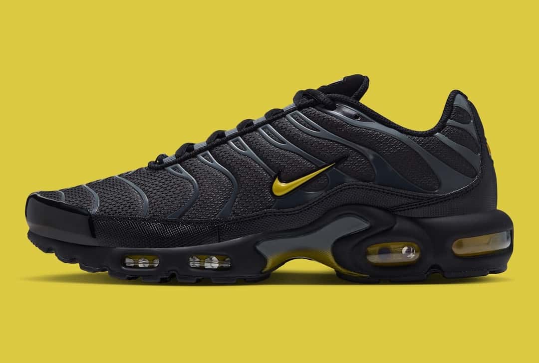 Nike Air Max Plus del pack Batman de perfil sobre fondo amarillo, con malla negra, jaula gris, Swoosh amarillo y cámaras de aire amarillas