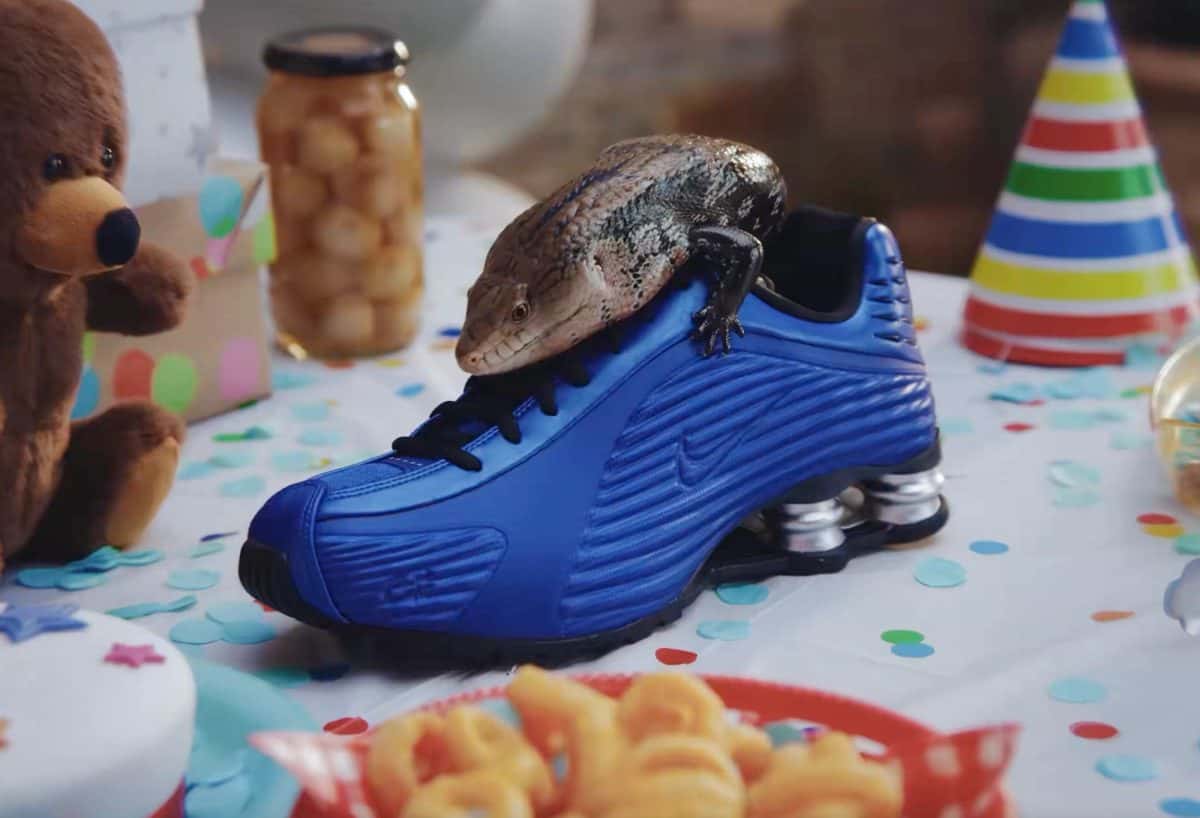 Corteiz x Nike Shox R419 azul Game Royal con un lagarto encima, sobre una mesa de cumpleaños con confites, gorros de fiesta y un oso de peluche