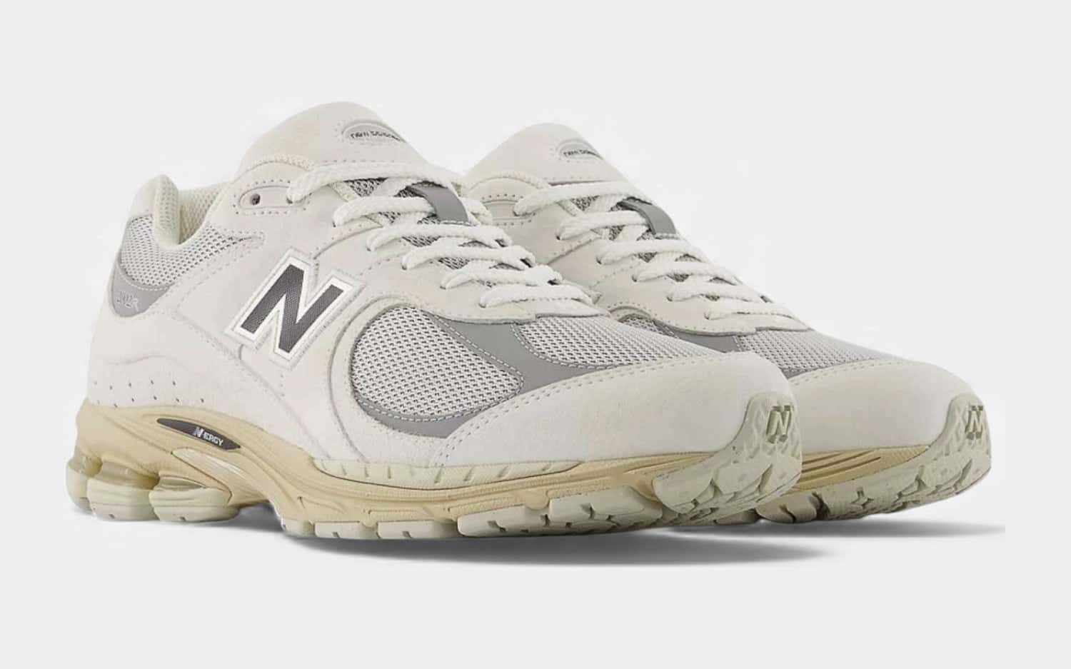Par de New Balance 2002R beige y gris claro con la N gris y la suela crema, sobre fondo gris