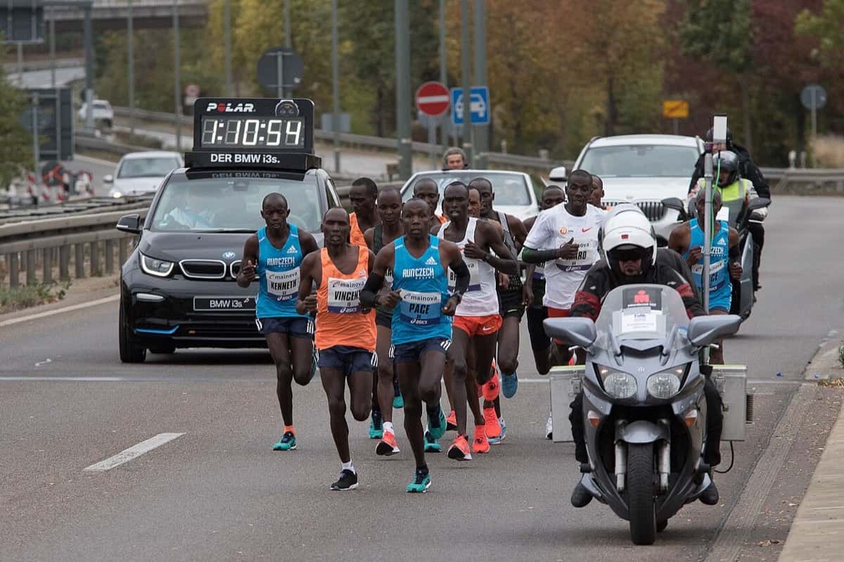 Foto de archivo: el grupo de punta del Maratón de Frankfurt 2018 corre por una avenida detrás de un auto con el reloj oficial y una moto de la organización