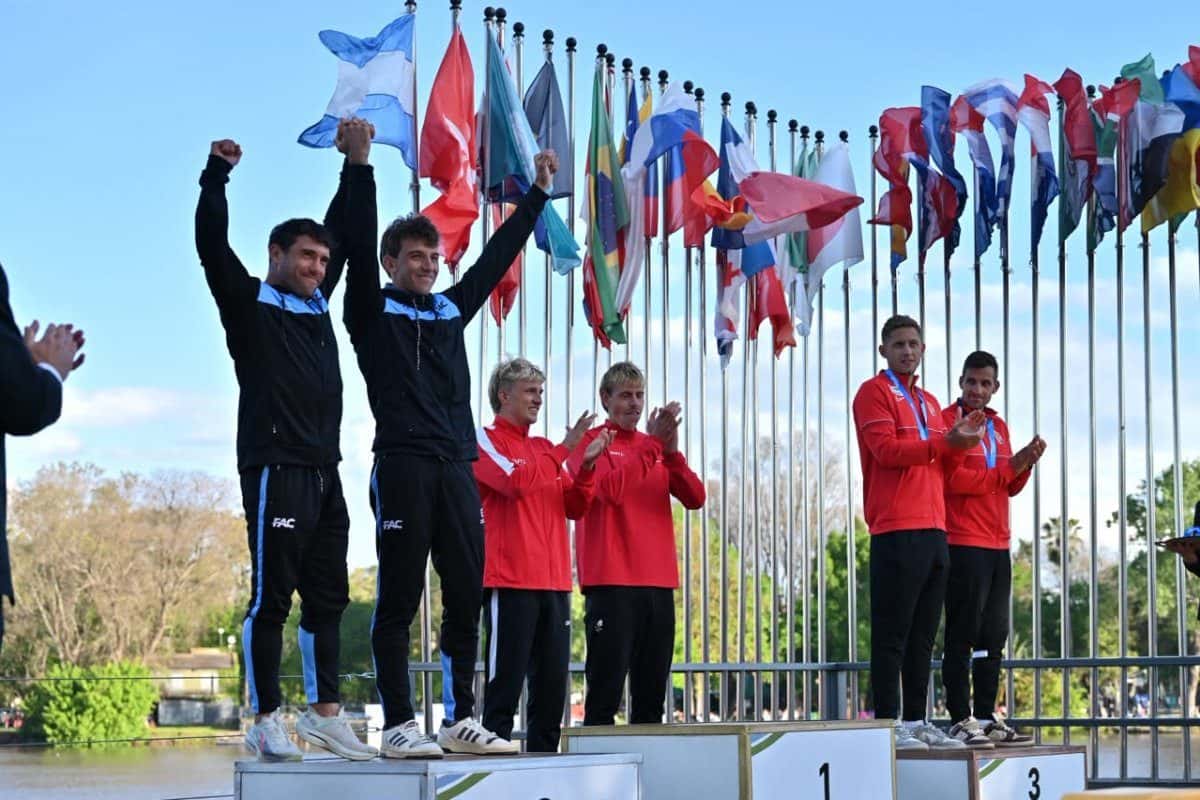Dos palistas argentinos, con campera negra y la medalla al cuello, levantan los brazos en el segundo escalón del podio del Mundial de Canotaje Maratón en Gualeguaychú