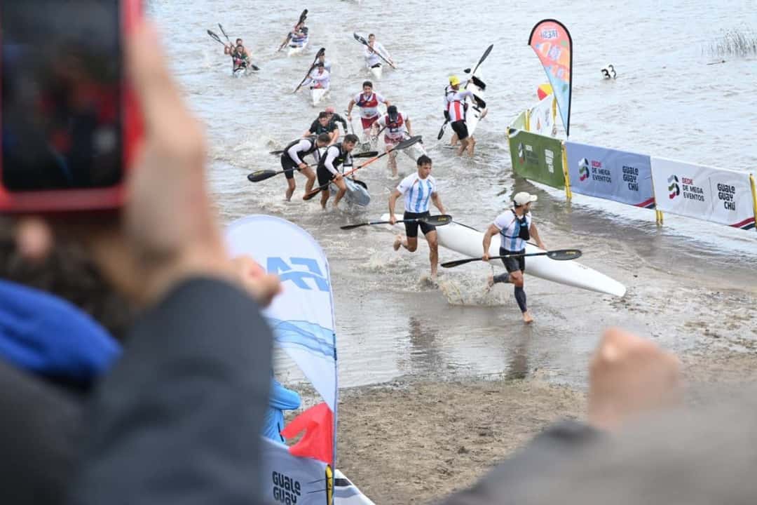 Palistas corren por la orilla con sus kayaks al hombro durante una prueba del Mundial de Canotaje Maratón, con público alrededor