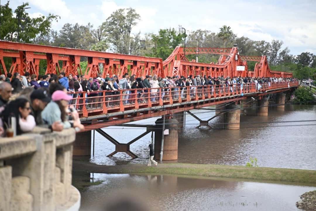 Una multitud mira la competencia desde un puente de hierro rojo sobre el río Gualeguaychú