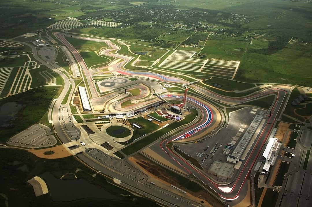 Vista aérea del Circuito de las Américas, en Austin, con la recta principal que sube hacia la curva 1, la torre de observación roja y las tribunas rodeadas de campo verde