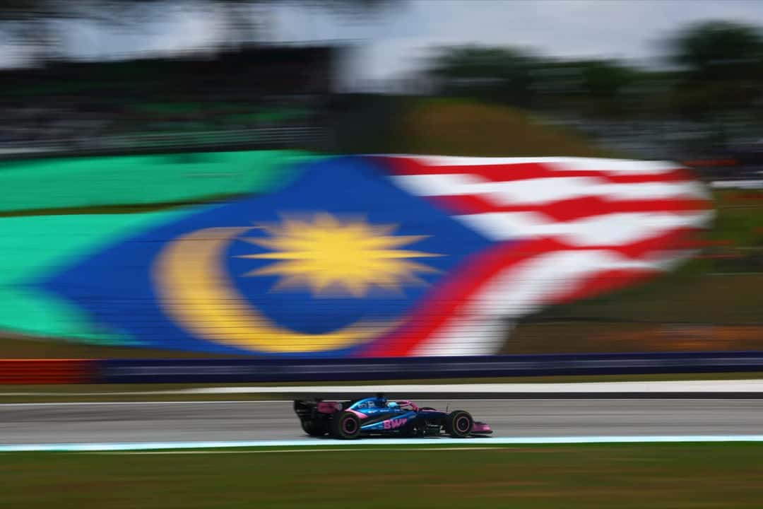 Un Alpine a toda velocidad en Sepang, con una gran bandera de Malasia pintada en la tribuna de fondo