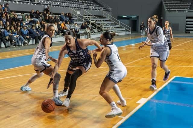 Una jugadora de Peñarol, con la camiseta azul a rayas, pelea la pelota en el piso entre dos jugadoras de Boca de blanco, en el Polideportivo Islas Malvinas