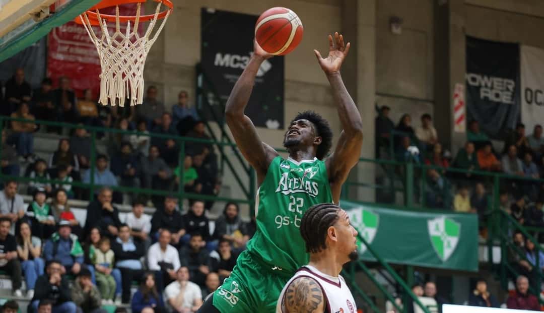 Un jugador de Atenas, con la camiseta verde número 22, lanza al aro ante la marca de un rival de Lanús