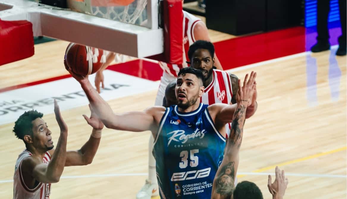 Un jugador de Regatas Corrientes con la camiseta azul 35 lanza una bandeja ante la marca de jugadores de Instituto con camiseta blanca y roja