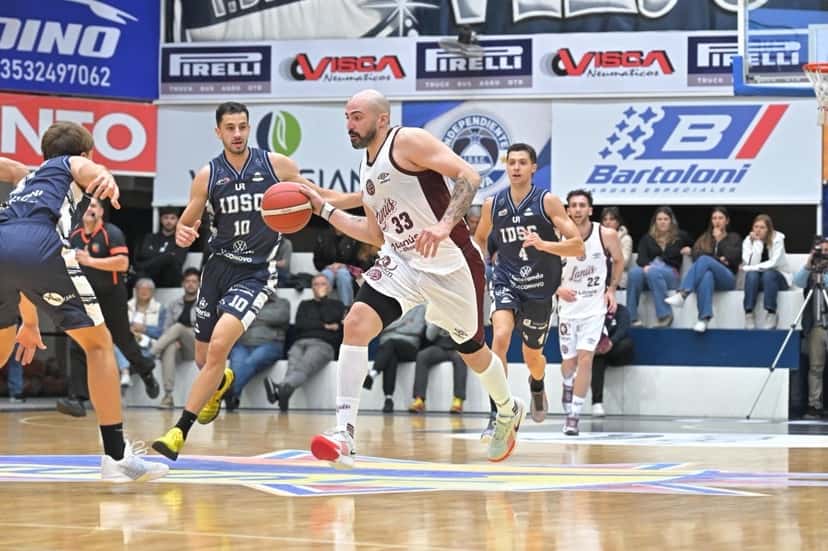 Un jugador de Independiente de Oliva, con camiseta azul oscuro, ataca con la pelota ante la marca de un jugador de Lanús, de blanco, en El Gigante de la Ruta 9