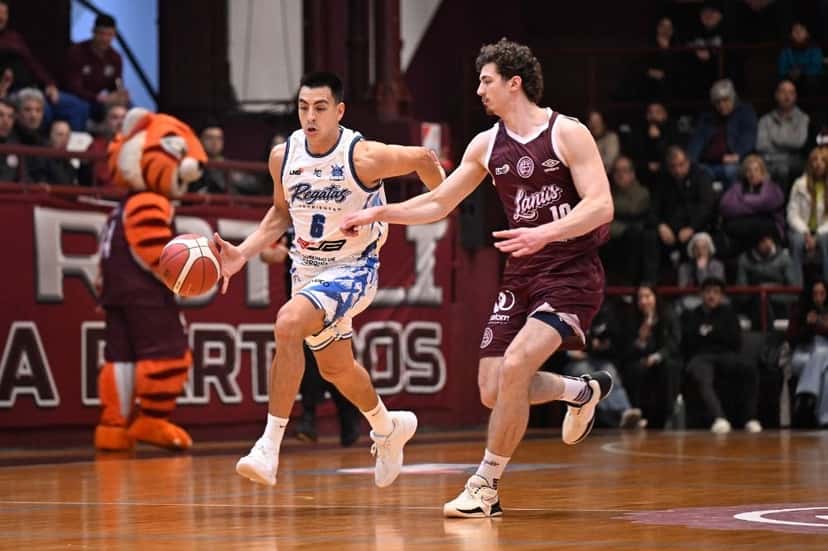 Un jugador de Regatas, de blanco con el número 6, conduce la pelota marcado por un jugador de Lanús, de granate con el número 10, en el Rotili