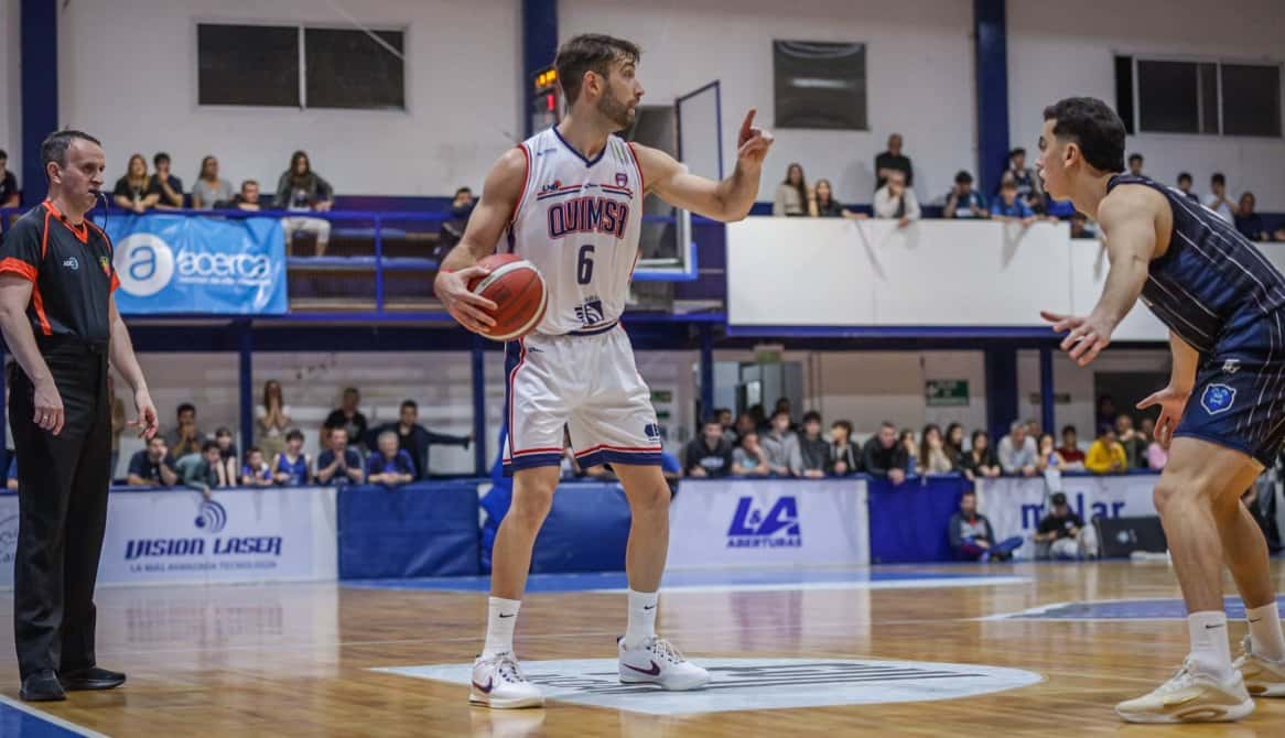 Un jugador de Quimsa, con camiseta blanca y el número 6, avanza con la pelota ante la marca de Argentino en el estadio de Junín