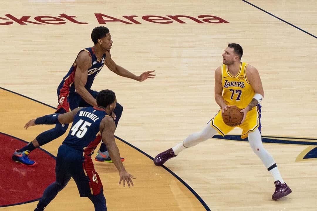 Foto de archivo: Luka Doncic, con la camiseta amarilla número 77 de los Lakers, sostiene la pelota frente a dos jugadores de los Cleveland Cavaliers, de azul